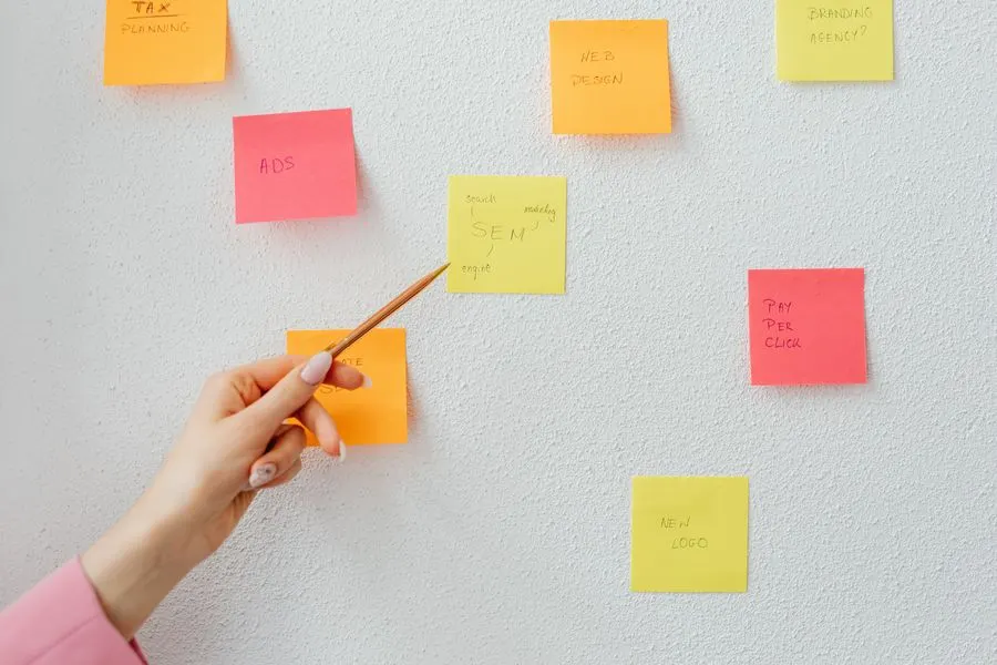 Une main désigne des notes autocollantes sur un mur